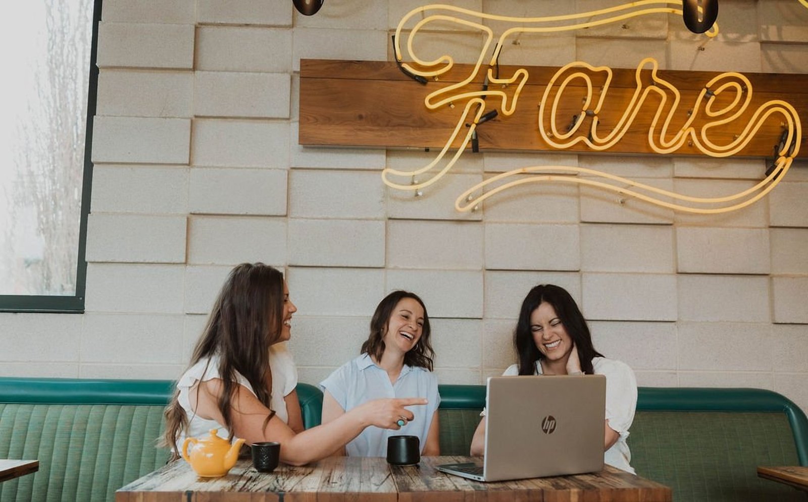 Erin, Keri and a designer laughing together at a table beneath a neon sign