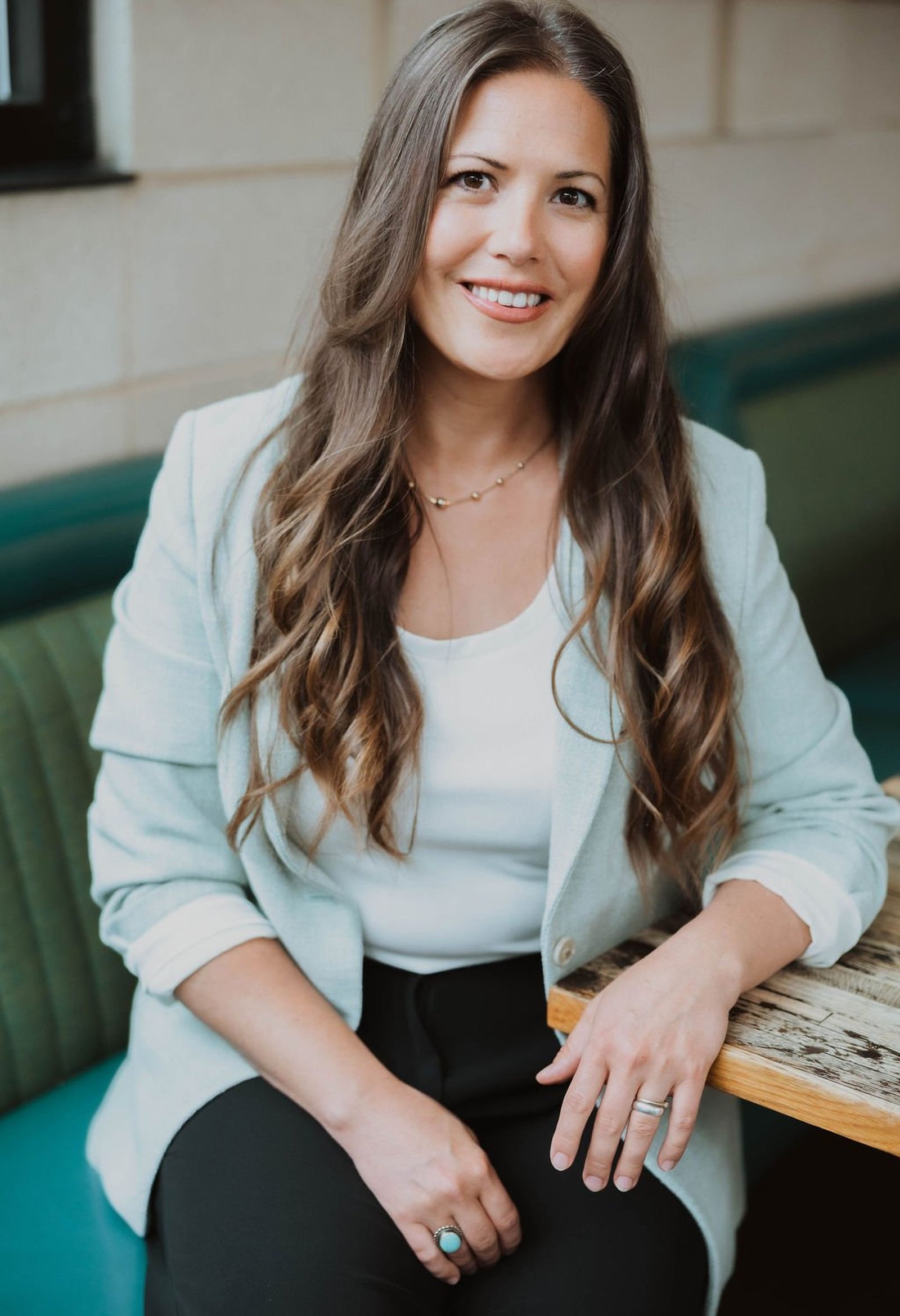 Erin Hildmann, co-founder of The Collective for Designers, smiling in a pale blue blazer on a teal banquette