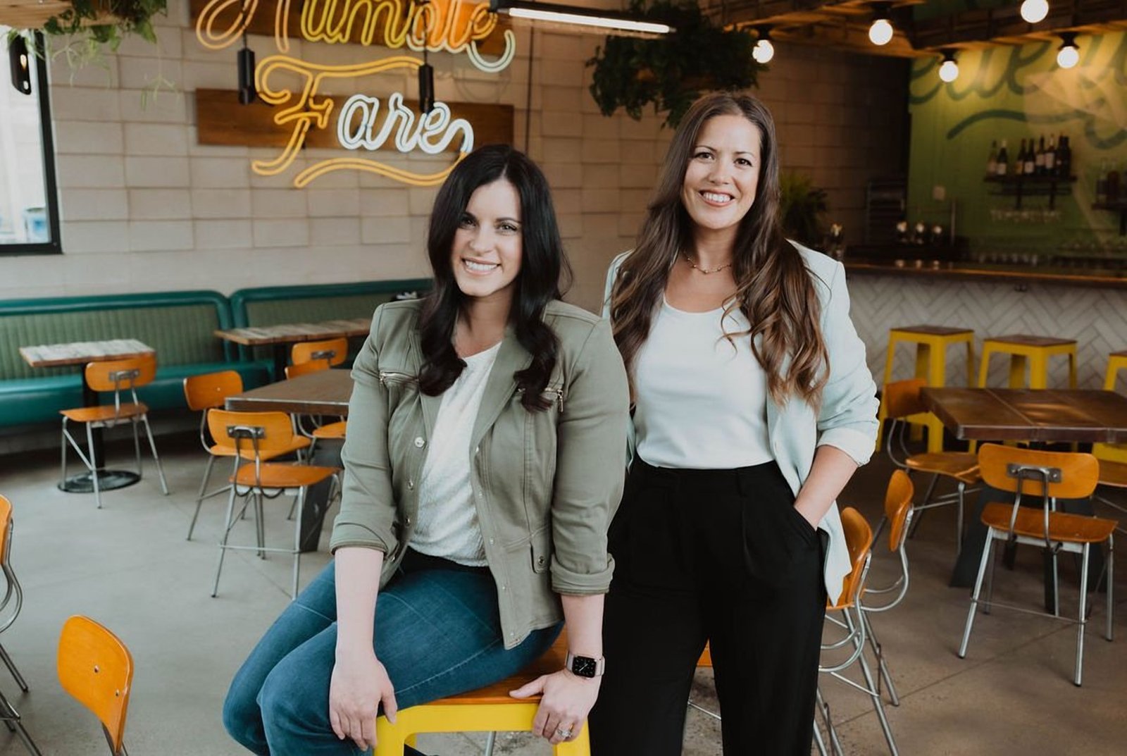 Keri and Erin standing together among yellow chairs at a Denver restaurant