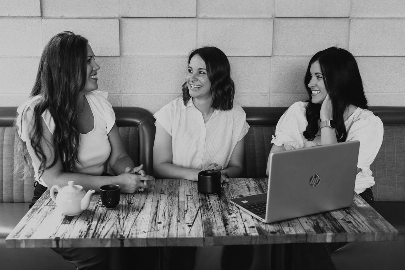 Black and white photograph of a designer laughing mid-conversation at a laptop